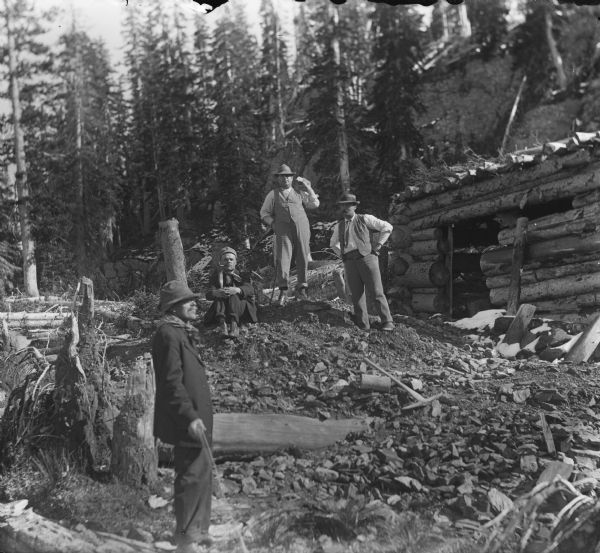 Men in the Leighton-Wyoming mining camp taking a break from clearing the area directly around a log cabin that is either in the process of being built or being destroyed. Harry Dankoler is in the foreground on the left holding the string to release the shutter on his camera.
