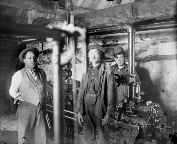 Three men are standing with machinery, likely a sawmill, peripherally related to the Leighton-Wyoming mining operation.