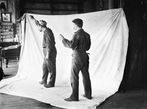 Two men standing in front of a backdrop pose for a photograph staged at Harry Dankoler's photography studio.