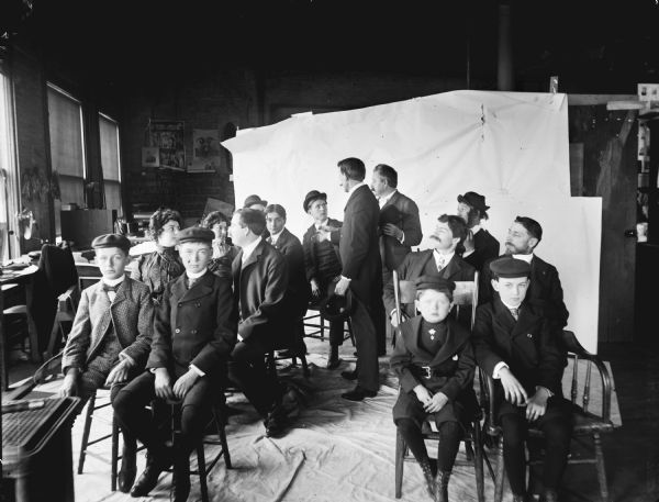 A large group of people posed in chairs at Harry Dankoler's photography studio. Syl is the youngest child on the front row near the center aisle on the right.