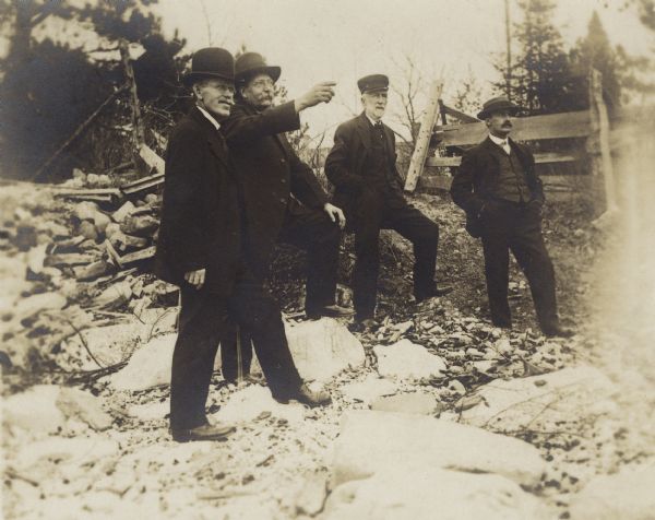 Harry E. Dankoler, E.A. Corneille, D.S. Crandall, and Joe Leighton standing on a rocky area of D.S. Crandall's property near a fence.