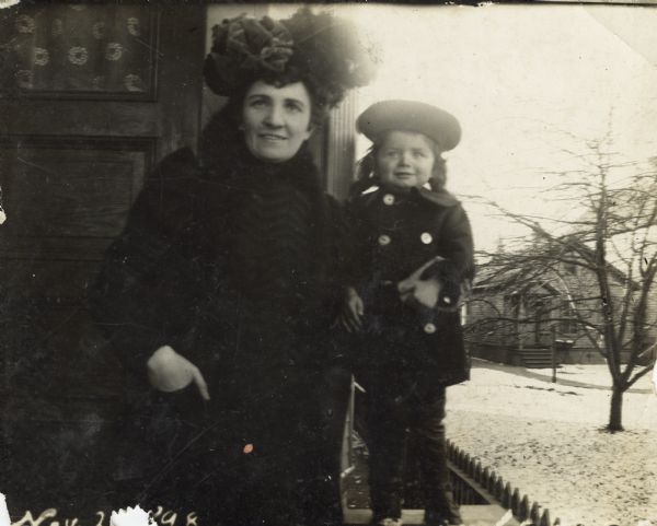 Aunt Helen and Syl stand bundled up against the cold just outside a door to a house with a snow-covered yard behind them.