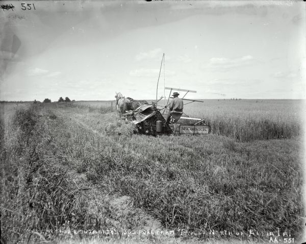 A man is operating a horse-drawn McCormick grain binder in a field.  In the distance a man and young boy are walking in the field. Text written on the glass plate is as follows: [FT? Work on Thos Dougherty's 1200 Acre Farm 7 miles north of Albia, IA]