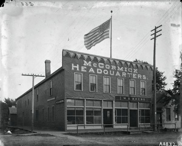 McCormick Harvesting Machine Company dealership or agency building of W.S. Krebs, possibly in or near Albert Lea, Minnesota. Lettering on the building reads "McCormick Headquarters," and a large American flag is flying above the building.