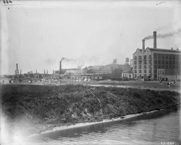View of what appears to be the McCormick Reaper Works, with the west fork of the south branch of the Chicago River in the foreground. Smokestacks, railroad cars and water towers are in the distance.