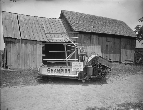 1900 Champion grain binder with a "For Sale" sign on it sitting in front of a barn. The sign on the machine reads: "1900 Champion Har. and Binder; No Good in Heavy Wheat - For Sale; $50; Walter Biebel, Belleville, Ill.