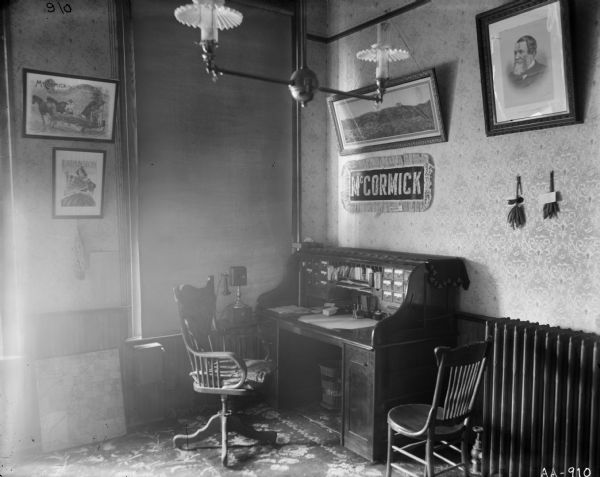 Office in a McCormick Company building — possibly a factory, branch house, dealership or office building. A desk, chairs, telephone, radiator, wastebasket, framed advertising posters and a portrait of Cyrus Hall McCormick are present.