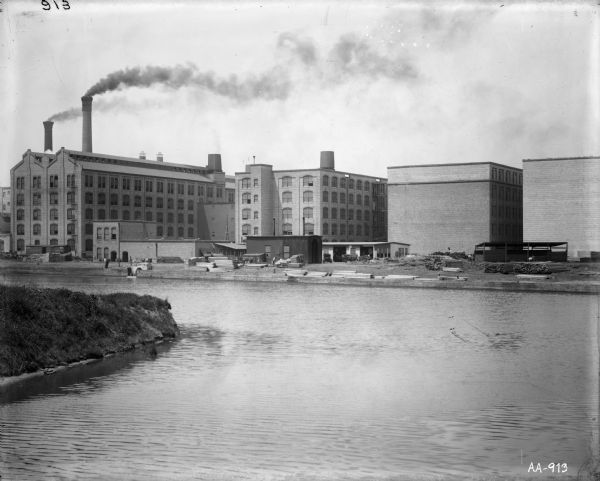 View of factory buildings and smokestacks from across a river or industrial canal. The factory is probably the McCormick Reaper Works as seen from across the west fork of the south branch of the Chicago River.