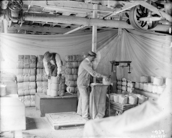 Factory workers in the weighing and sacking room at the McCormick Twine Mill. A scale is standing in the background at right. White sheets are hanging in the background as backdrops.