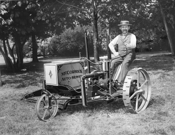 A well-dressed man is sitting in the seat of a McCormick Auto-Mower, possibly at the Paris Exposition. The experimental machine is thought by some to be the first gas-powered tractor.