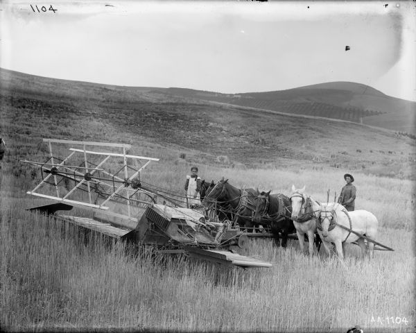 A man and girl posing in a field with a horse-powered push binder. Hills are in the background.