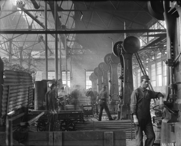 Factory workers standing amid machinery in the forge shop at the McCormick Reaper Works.