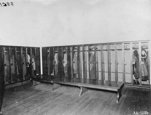 Rows of lockers with screen doors, probably at the McCormick Works. Some of the lockers contain hats, shoes, and coats. A long bench runs along the wall of lockers.