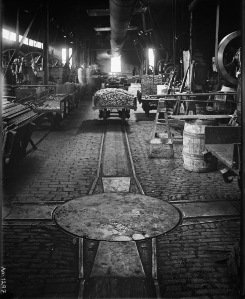 Rails or tracks in a factory floor, probably at the McCormick Reaper Works, with machines, a cart loaded with lumber, and ghostly images of workers in the distance.