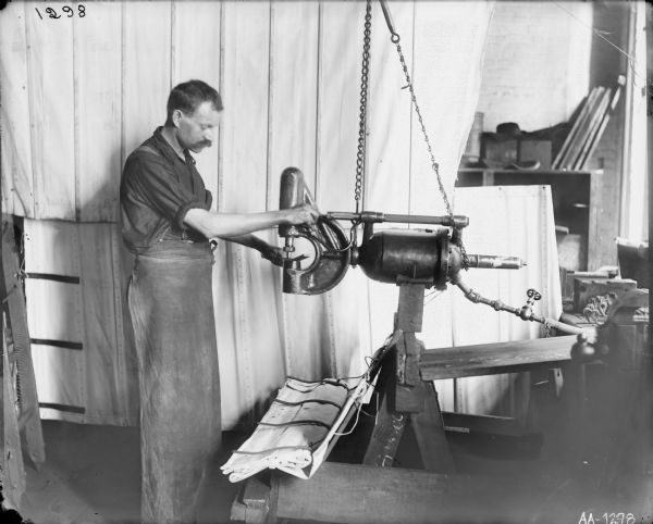 Factory worker operating a drill press or punch, probably at the McCormick Reaper Works. The worker is standing against a backdrop of canvas sheets and there appears to be canvas at his feet. The canvas may have been intended for grain binders.