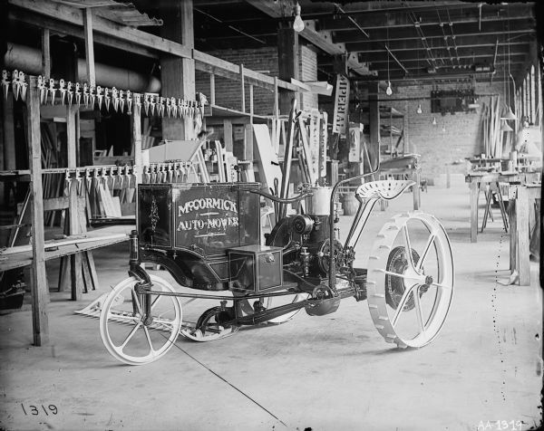 McCormick "Auto-Mower" on the floor of a shop or factory. The Auto-Mower was an experimental engine powered mower that won first prize at the Paris Exposition of 1900. This is one of two Auto-Mowers produced by the company. This machine had a single-cylinder engine. The other machine had a two-cylinder engine.