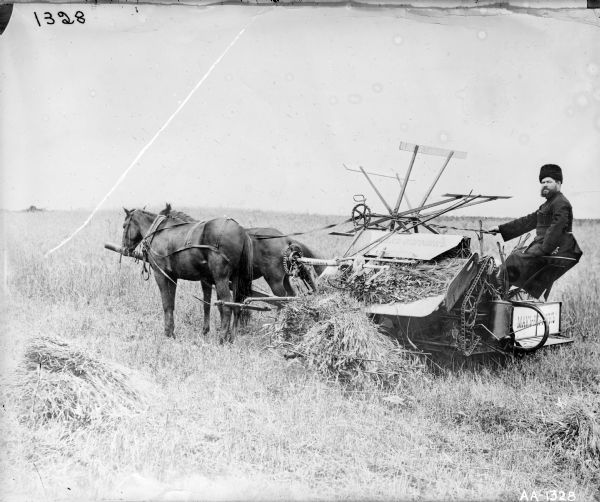 Farmer sitting in the seat of a horse-drawn McCormick grain binder, probably in Russia. The "McCormick" name on the binder appears in Russian.