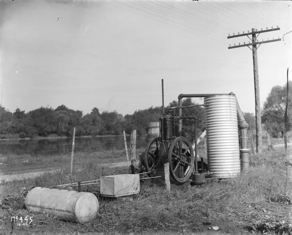 An International Harvester stationary engine appears to be powering a water pump, perhaps for irrigation. In the background is a pond.