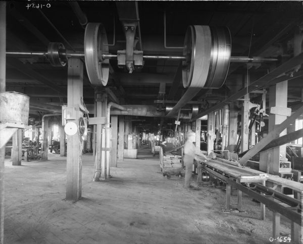 Factory workers saw lumber from a cart at International Harvester's Osborne Works. To the left on one of the beams saw blades are hanging. The belt-driven machinery is attached to the ceiling.