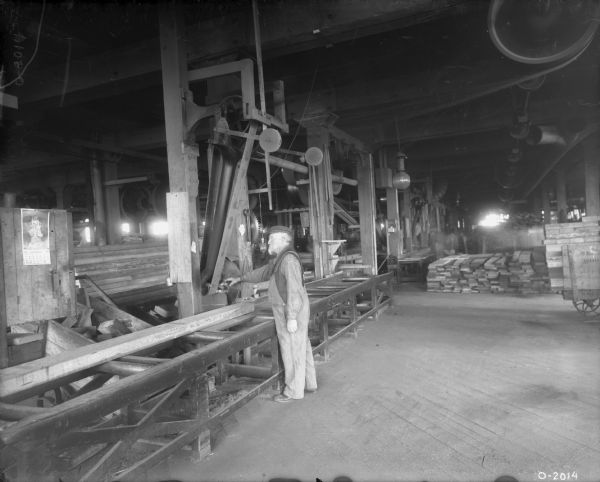 Factory worker sawing a large piece of lumber at International Harvester's Osborne Works (later known as "Auburn Works"). The belt-driven machinery is along the ceiling.