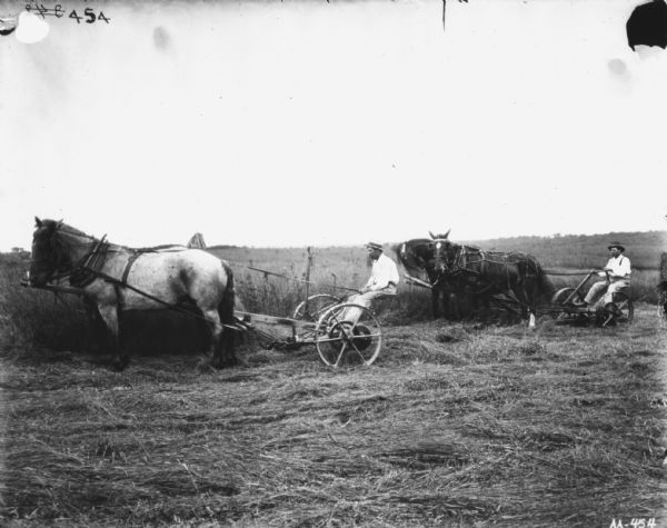 Left side view of two men in a field using horse-drawn mowers.