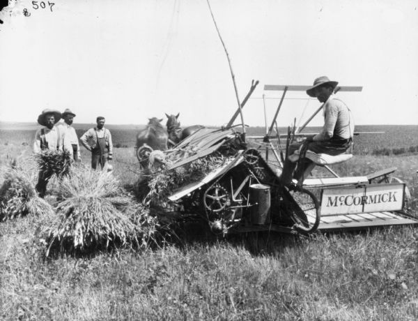 Three men are standing near a man (Ray Clark?) using a horse-drawn McCormick binder in a field.