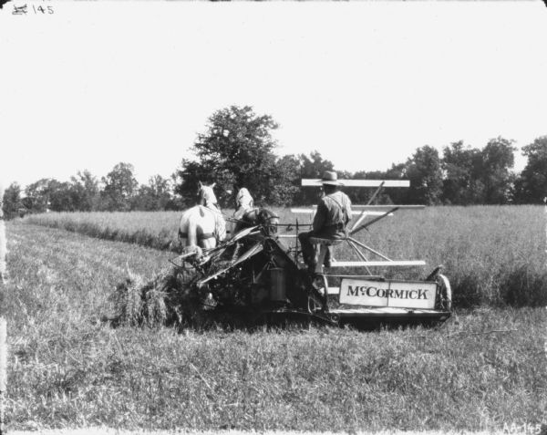 Rear view of a man using a horse-drawn McCormick binder in a field.