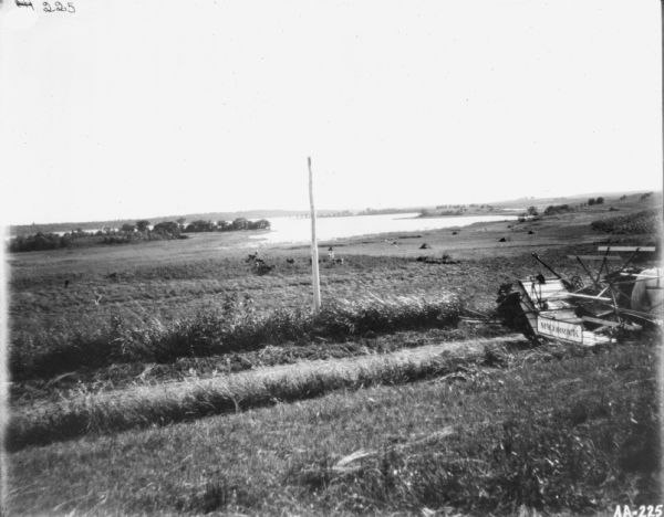 View down hill towards a horse-drawn binder on a road. In the background is a large body of water.