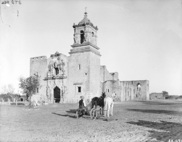 Rear view of a man on a horse-drawn mower. In the background are the ruins of a large building, probably a church.