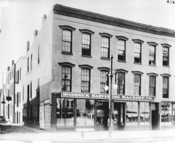 View from street of the H.R. Thurber dealership. There is an alley on the left. The sign above the door on the left reads: "H.R. Thurber, Gen." and the sign above the doorway on the right reads: "Central-Union Transfer-Storage Co." A large lamppost is on the sidewalk in front.