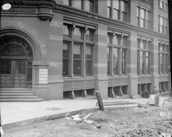 Construction in the street in front of the McCormick Harvesting Machine Co. building at 212 Market Street. On the far right a man is standing and working on a large stone near the curb.