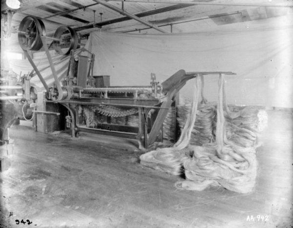 Manila fiber feeding into manufacturing machine. The manila is pooled on the floor. A white sheet is hanging in the background as a backdrop.