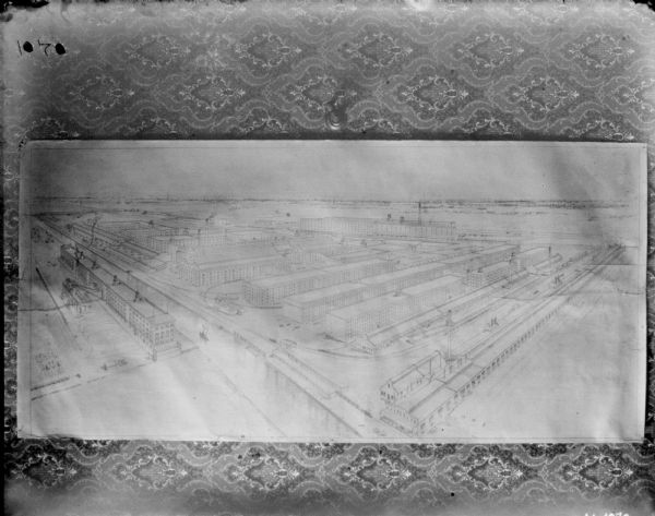 Drawing of factory buildings, seen from an elevated view. The drawing appears to be attached to a wall with wallpaper.