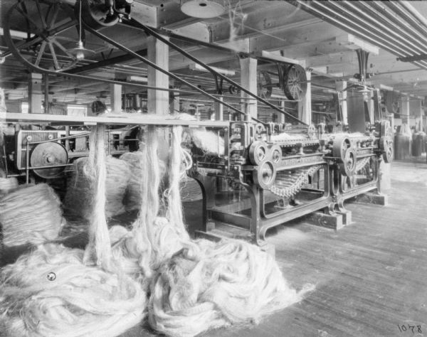 Bales of twine next to a manufacturing machine at McCormick Works. Coils of manila are fed into the machine, which is belt-driven from the ceiling.
