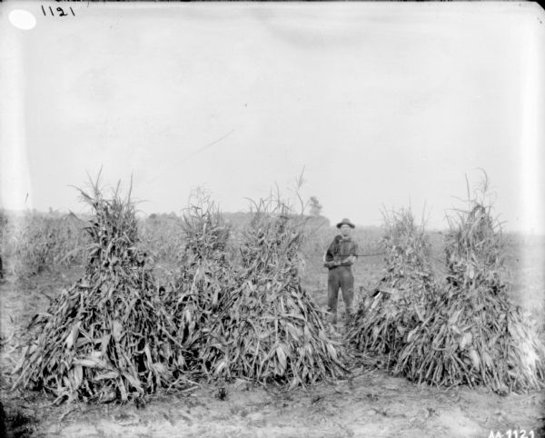Portrait of a man holding a dog while posing behind shocks of cornstalks.