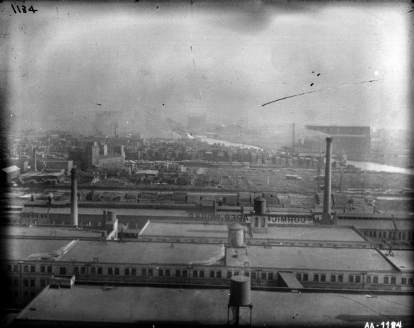 Elevated view over rooftops of the McCormick Works. Beyond the rooftops is a lumber yard. A river is in the background.