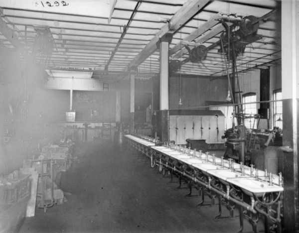 View of wash room at McCormick Works. In the middle of the room is a double row of wash sinks. In the background are lockers. On either side of the sinks are various pieces of belt-driven machinery.