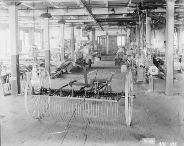 Dump rake on factory floor. In the background on the right is belt-driven machinery.