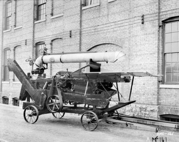 Thresher outdoors in front of factory building at McCormick Works.