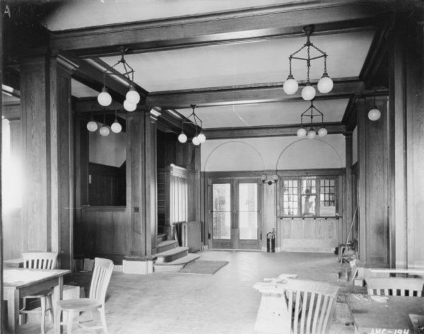 Interior view of lobby. There are tables and chairs in the foreground. In the background on the left is a flight of stairs. In the center is a set of double doors, and on the right is the cashier's window.