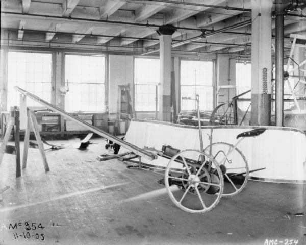 Mower set up on factory floor in a factory. In the background are other pieces of agricultural machinery, and a bank of windows.