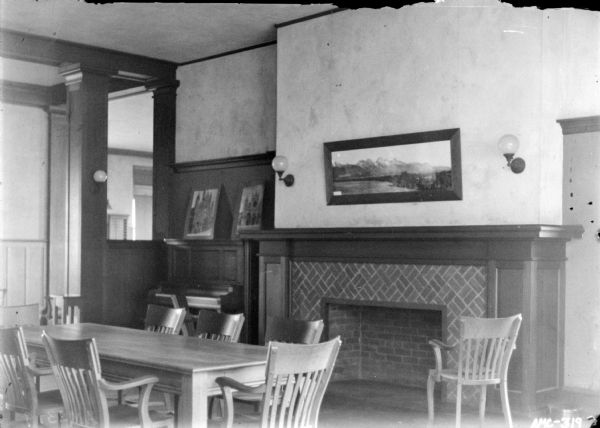 Interior view of the reading room at the club house. There is a table with chairs in front of a fireplace. There is a piano in the corner.
