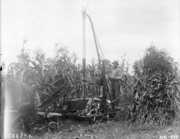 View of a man standing on a platform binding corn stalks in a field.