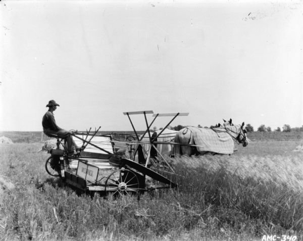 Right side view of a man using a horse-drawn McCormick binder in a field. The three horses are wearing blankets and blinders.
