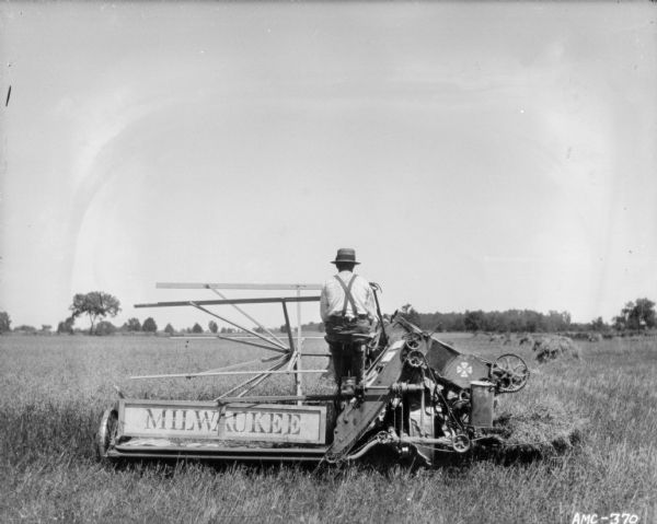 Rear view of a man using a horse-drawn Milwaukee binder in a field.