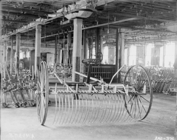 Dump rake on factory floor. Other agricultural parts and implements are in the background.