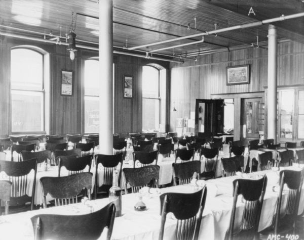 Dining room in the club house, looking over tables towards a row of windows. In the back corner is an open door to the kitchen.