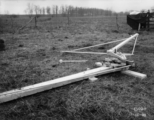 Power section of a horse-powered Hay Press outdoors in a field. There is a horse behind a fence in the background on the right.