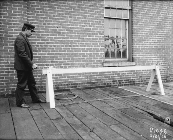 Man stretching baling wire next to a brick building.
