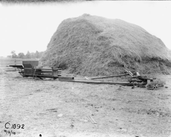View across field towards a hay press near a large haystack.